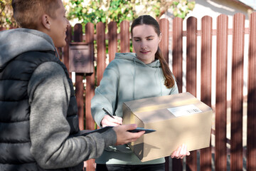 Woman signing papers while receiving parcel from postman outdoors