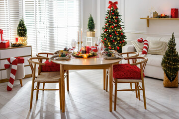 Christmas table setting with stylish dishware, glasses and burning candles in festive decorated room