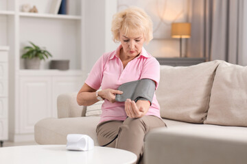 Fototapeta premium Senior woman measuring blood pressure on sofa at home