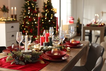 Christmas table setting with stylish dishware, glasses and burning candles in festive decorated room