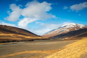 Golden valley surrounded by snowy peaks, with a meandering river cutting through the vast, open landscape under a bright sky.