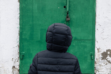 A boy in a hood in front of a closed green door with a padlock