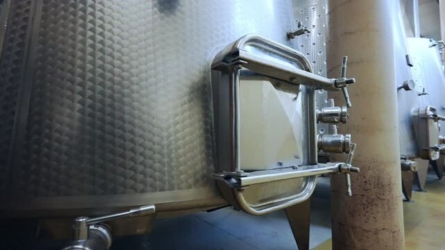 Metal tank with small central gate, some taps, pipes and grade regulators for wine making, factory with lots of stainless barrels for high quality wine storage, viticulture industry
