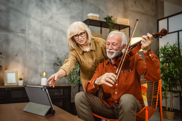 senior man learn to play violin at home on tablet and wife support him