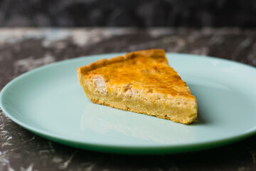 Piece of delicious open pie quiche with chicken, cheese and cream on a turquoise plate, copy space. Food blog concept, recipe writing.