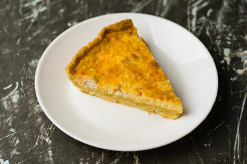 Flatlay, a piece of delicious open-faced quiche pie with chicken, cheese and cream on a white plate. Concept of food blog, writing recipes.