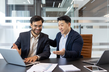 Male mentor at workplace helping intern learn new work project, two men in business suits working...