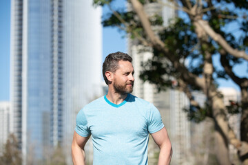 Fototapeta premium Outdoor male portrait. Man in blue t-shirt posing near American city. Happy business man posing outside. Businessman. Business man in t-shirt. American owner, casual businessman.
