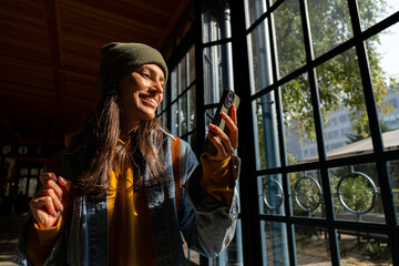 A joyful woman leaning against a sunlit window, using her phone to look up information about the exotic plants showcased in the botanical garden.