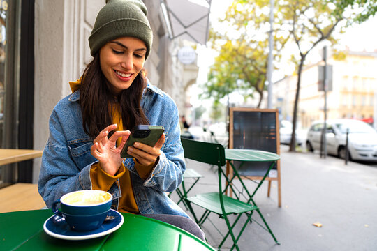 Smiling woman at a coffee shop, looking at her phone and relaxing with a cup of coffee