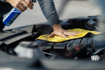 Close up of man's hands cleaning under the car hood with rag and spray.
