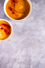 Two bowls with pumpkin soup with paprika spices and cream on white table. Flat lay with copy space. Cream soup. Concept of tasty healthy food.