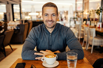 Portrait of a smiling man sitting in coffee shop with coffee in front of him.