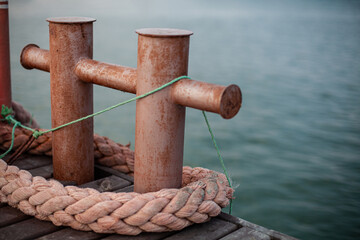 Rusty bollards on a dock with thick ropes and green string, close-up of weathered metal, showcasing nautical and maritime equipment in a harbor setting.
