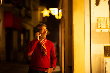 Smiling man on city street at night holding phone and looking at store display