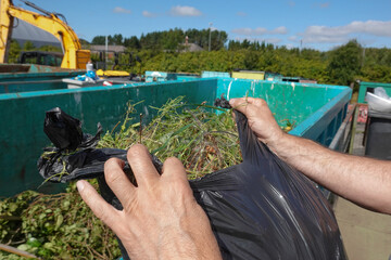Person tipping garden waste into a recycling bin, recycling centre