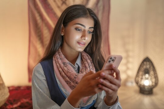 Sch&ouml;ne junge Inderin schaut aufmerksam auf ihr Smartphone. Innenaufnahme bei schwachem Licht