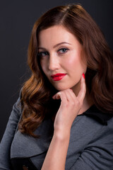 Portrait of a beautiful smiling young woman with auburn hair, hand on chin and wearing a vintage style grey dress, against a dark studio background.