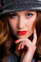 Portrait of a beautiful young woman with her hand on her chin, wearing a vintage style felt cloche hat against a dark studio background.