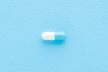 White blue pill on light blue table background. Closeup. Pastel color. Receiving vitamins or medicaments. Top down view.