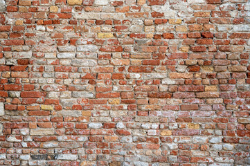 Brick wall with pieces of plaster. Wall of an old building in need of renovation. Aged wall texture of brick building close up. Grunge background with red and white blocks and layers of cement stucco