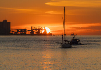 Vibrant sunset over Tagus River in Lisbon, Portugal, featuring dock silhouettes and sailboats in a calm and orange-toned seascape