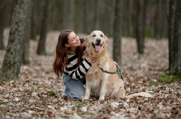 Teenage Girl Sits With Golden Retriever In Park During Autumn