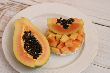 Papaya half and papaya slices on the white plate on the wooden background
