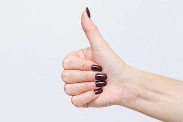 Thumb up gesture. Woman with beautiful manicure fingernails. Hand isolated on a gray background....
