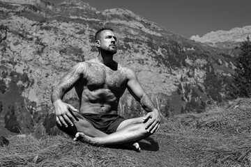 Latin Man meditating in lotus pose in grass outdoors. Sportsman doing yoga asanas meditating in city park. Athletic male meditating, relaxation, concept of healthy lifestyle. Outdoor meditating.