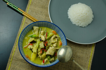Thai Green Chicken Curry with rice in a bowl on a black table, top view