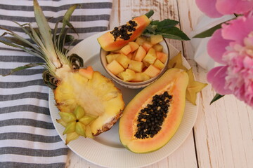 Fresh pineapple and papaya halves and carambola slices on the white plate on the wooden background