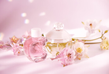 Two elegant cosmetic bottles, one pink and one clear, surrounded by soft pink and white flowers on a pastel pink background. Ideal for beauty, skincare, or wellness themes showcasing femininity 