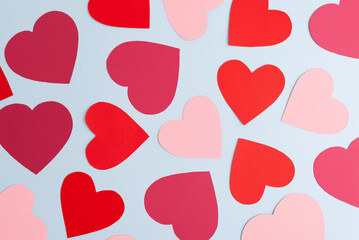 Red and pink paper hearts of various size lying on pastel blue background. Valentines Day, love and feelings concept