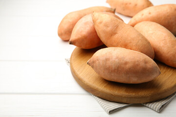 Fresh raw sweet potatoes on white wooden table, closeup. Space for text