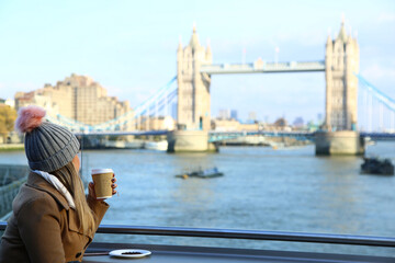 Girl drinking coffee looking to London Bridge, England