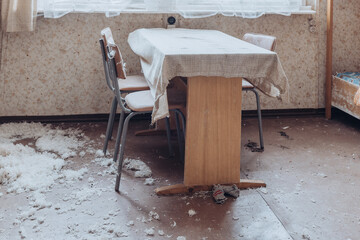 Abandoned interior of a room with a wooden table and scattered debris during daylight