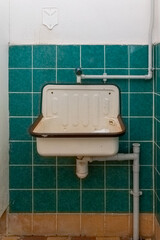 Wall-mounted sink in a tiled restroom with simple plumbing design during daylight hours