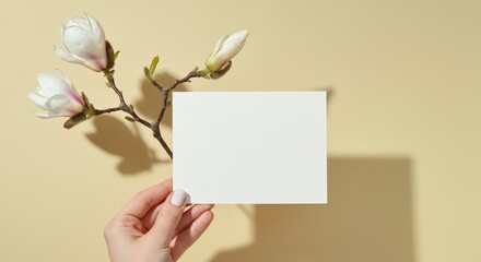 Obraz premium Hand holding a blank card next to a magnolia branch on a yellow background