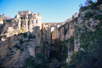 Puente Nuevo bridge connecting two sides of El Tajo gorge in Ronda, Malaga, Andalusia, Spain, during a sunny winter day with picturesque buildings and a waterfall