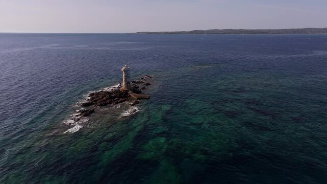 Sardinia&rsquo;s Faro Mangiabarche lighthouse, perched on brown rocks, surrounded by blue seas and soft waves.
