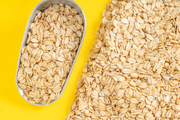 Metal scoop filled with raw rolled oats on a vibrant yellow background, ideal for healthy eating and diet concepts.