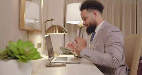 A successful businessman in an elegant suit sits at his modern desk, smiling while engaging with his laptop in a stylish office that reflects his career achievements and personal motivation
