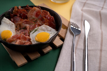 photo Delicious Breakfast with Crispy Bacon and Sunny-Side-Up Eggs in Cast Iron Skillet with Garnish and Cutlery on Linen for Perfect Start to Your Morning