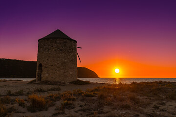 Kolorowy zachód słońca  z widokiem na stary wiatrak nad morzem na piaszczystej plaży, grecka wyspa Lefkada, krajobraz © anettastar