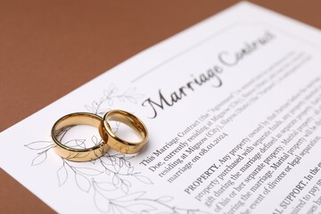 Marriage contract and golden rings on brown background, closeup