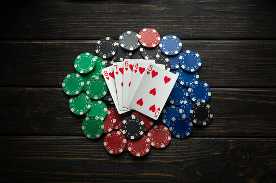 A pile of winning chips on a black table and playing cards lying on it with a winning combination in straight flush poker. Concept of luck in a casino or men club.