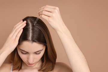Fototapeta premium Hair loss problem. Girl applying serum onto hairline on beige background, closeup