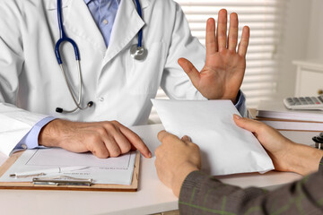 Corruption concept. Woman giving envelope with money to doctor at white table, closeup