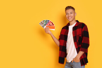 Portrait of young decorator with color palettes on orange background, space for text